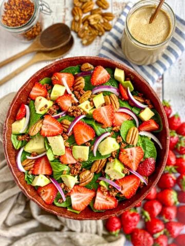 Spinach avocado strawberry salad in bowl with dressing on the side.