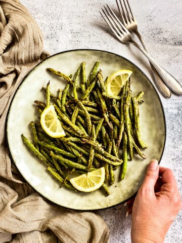 Air fryer green beans on plate with lemon wedges.