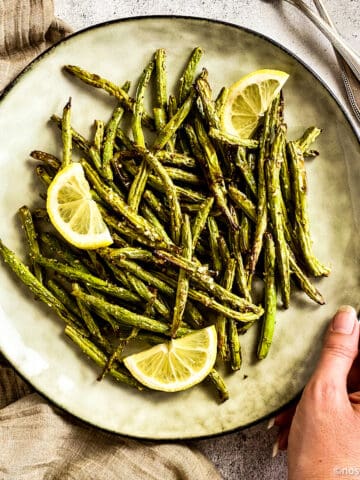 Air fried green beans on plate with lemon wedges.