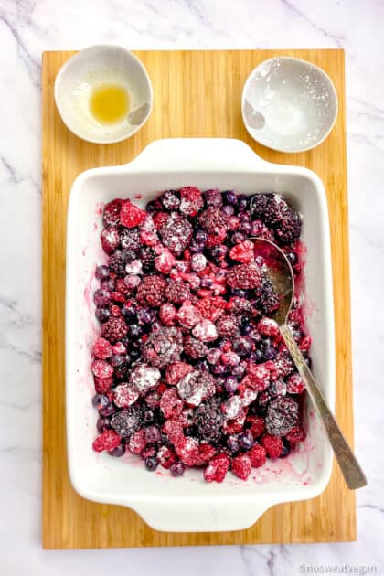 Baking dish with frozen berries mixed with cornstarch, maple syrup, and lemon juice.