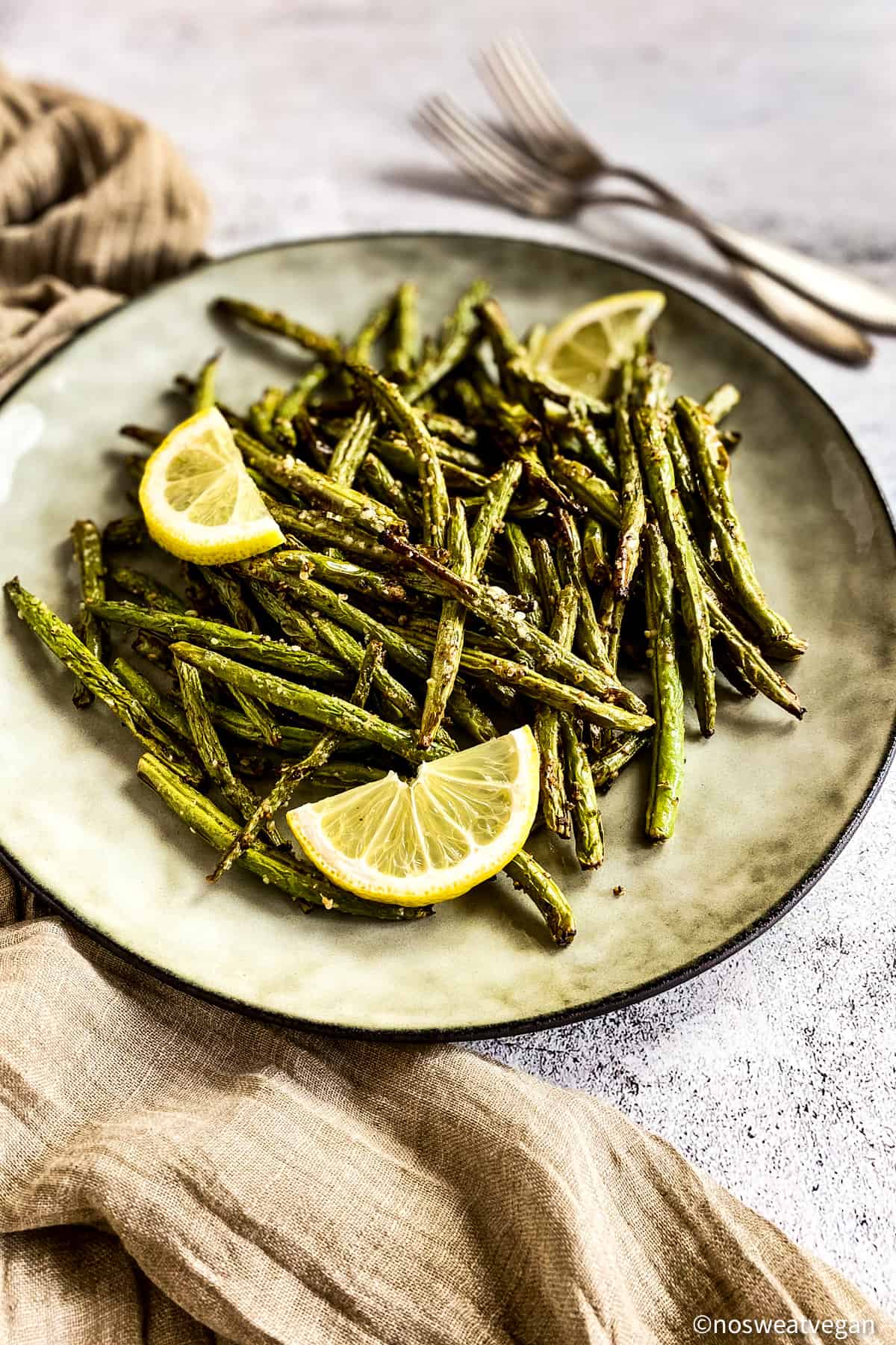 Green beans cooked in the air fryer on plated with lemon wedges.