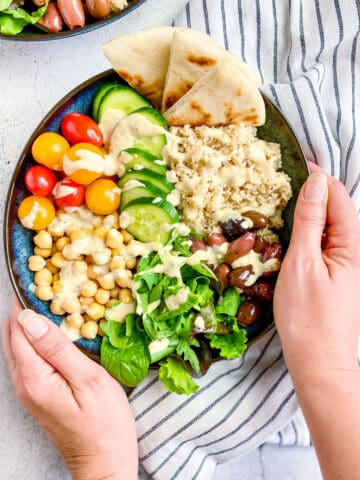 Two hands holding a vegan greek buddha bowl.