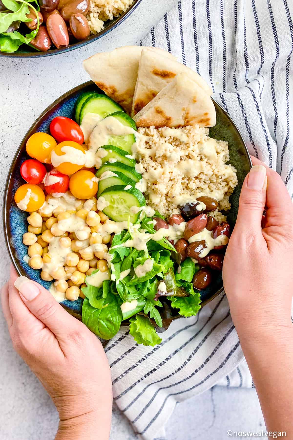 Two hands holding a vegan greek buddha bowl.