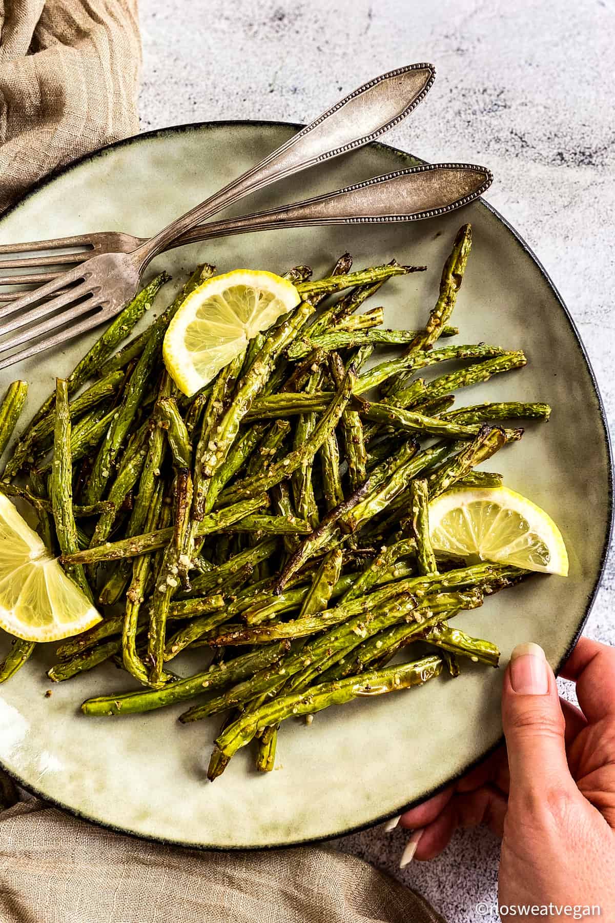 Air fryer green bean fries on plate with lemon wedges.