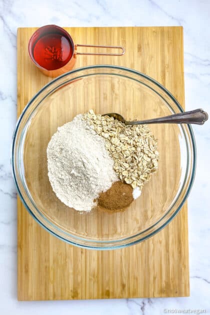 Bowl with flour, oats, cinnamon, and salt. Maple syrup in a measuring cup.