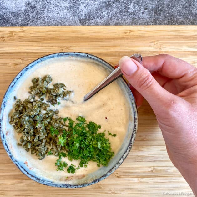 Hand about to mix parsley and capers into the vegan remoulade.