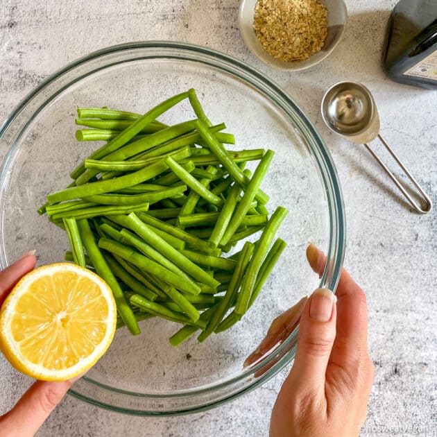 Bowl with trimmed fresh green beans. Hand holding half a lemon.