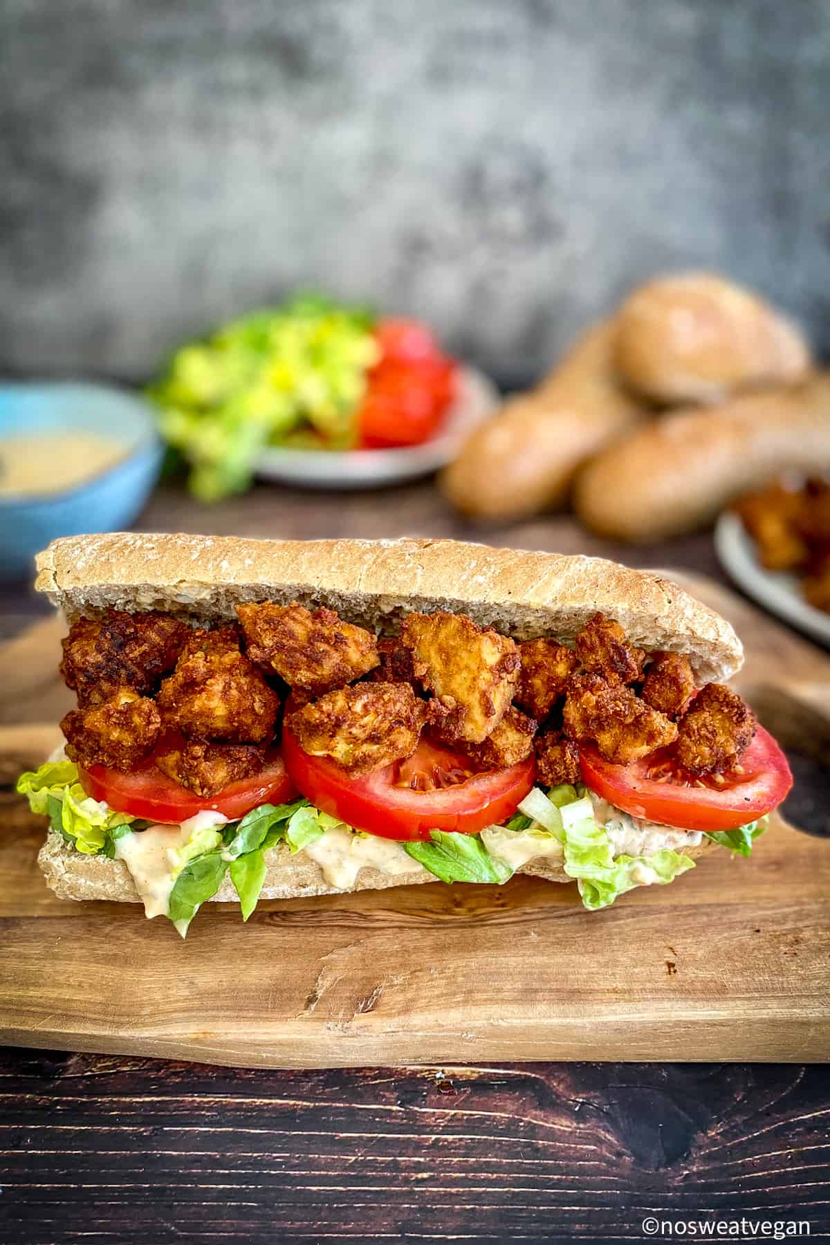 Tofu Po Boy on a cutting board with ingredients in the background.
