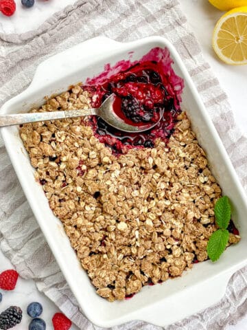 Vegan berry crisp in a baking dish with a spoon.