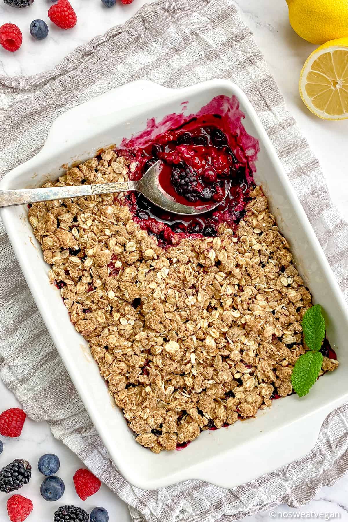 Vegan berry crisp in a baking dish with a spoon.