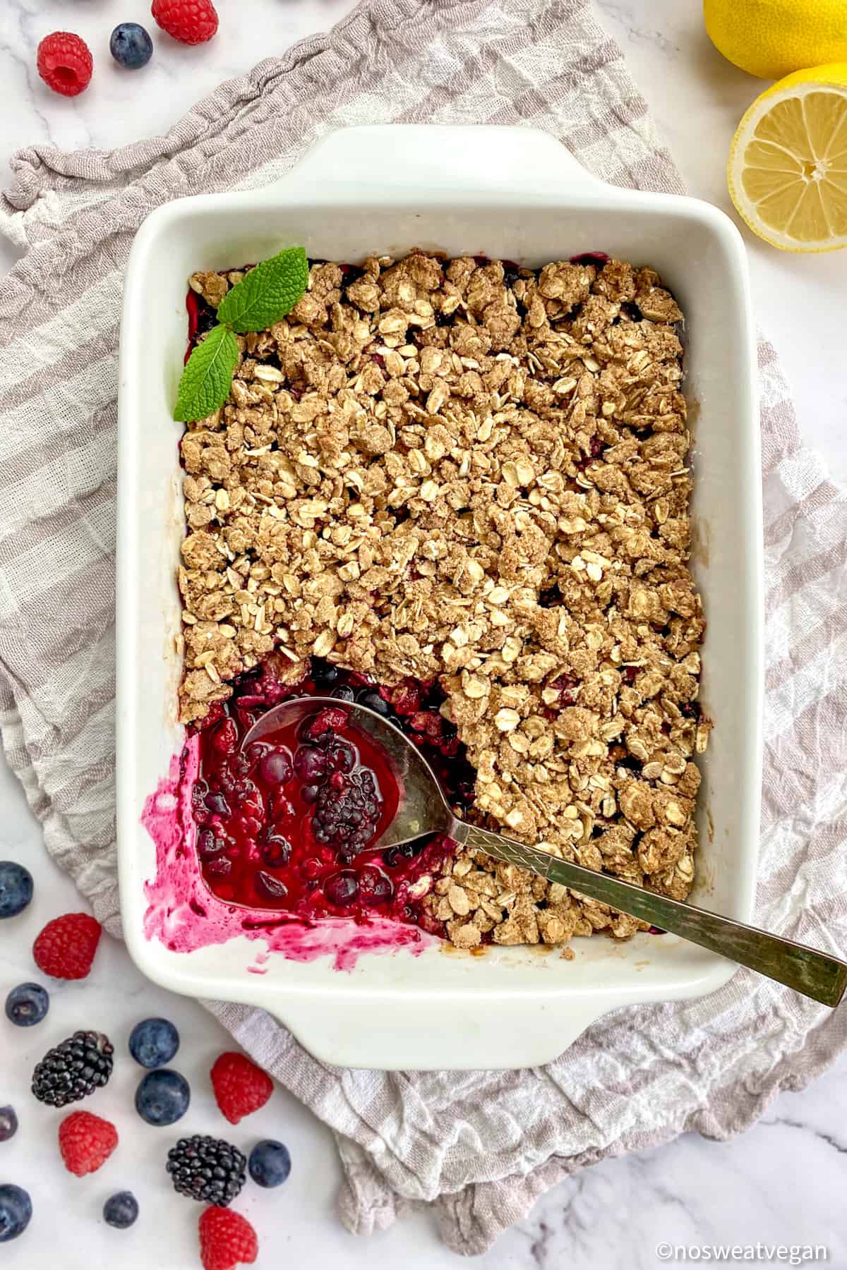 Vegan berry crumble in baking dish with corner scooped out to show mixed berry filling.