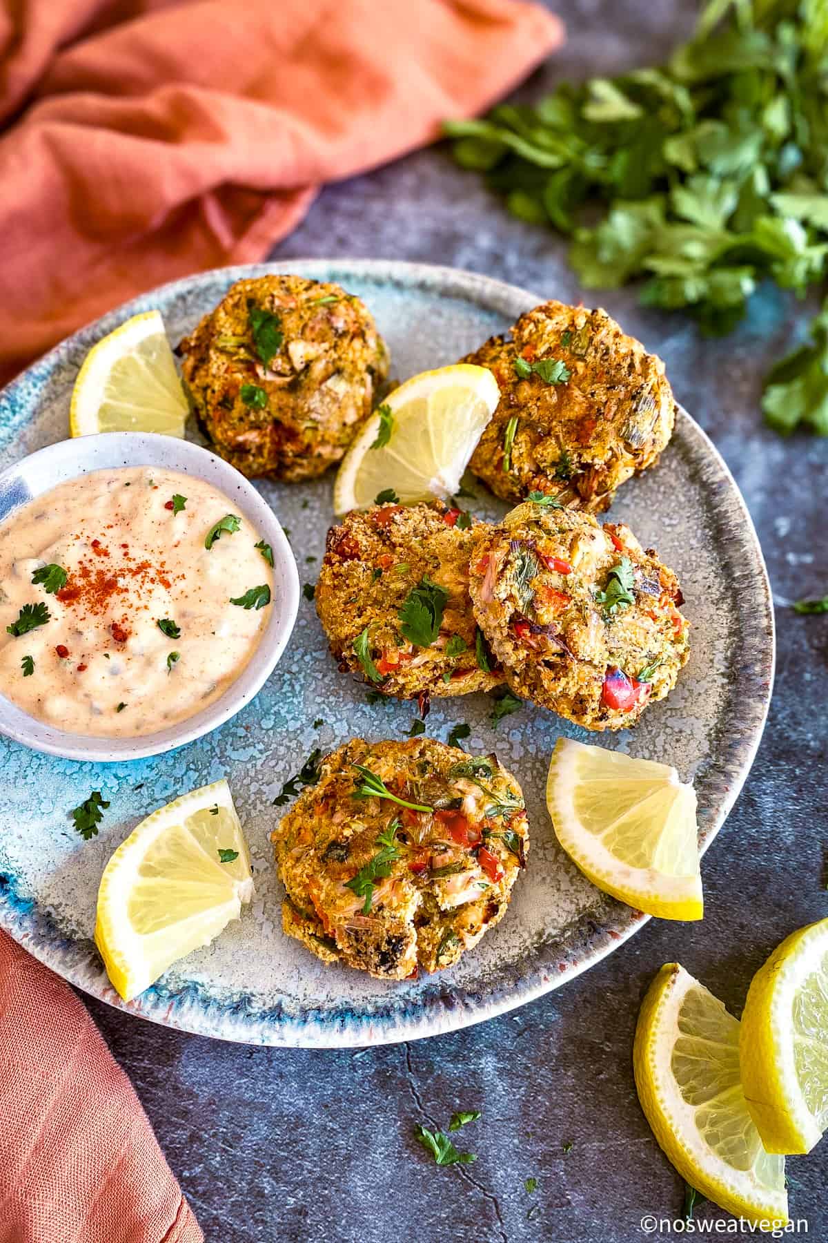 Vegan crabless cakes on plate with sauce and lemon wedges.