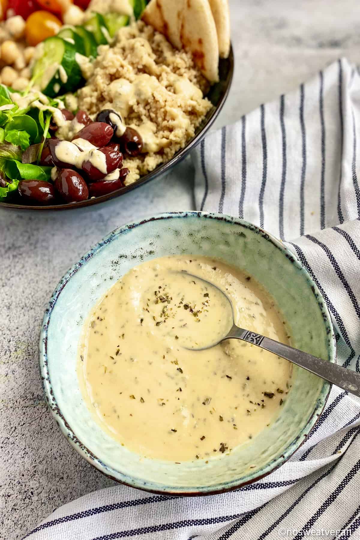 Hummus salad dressing in bowl next to Greek buddha bowl.