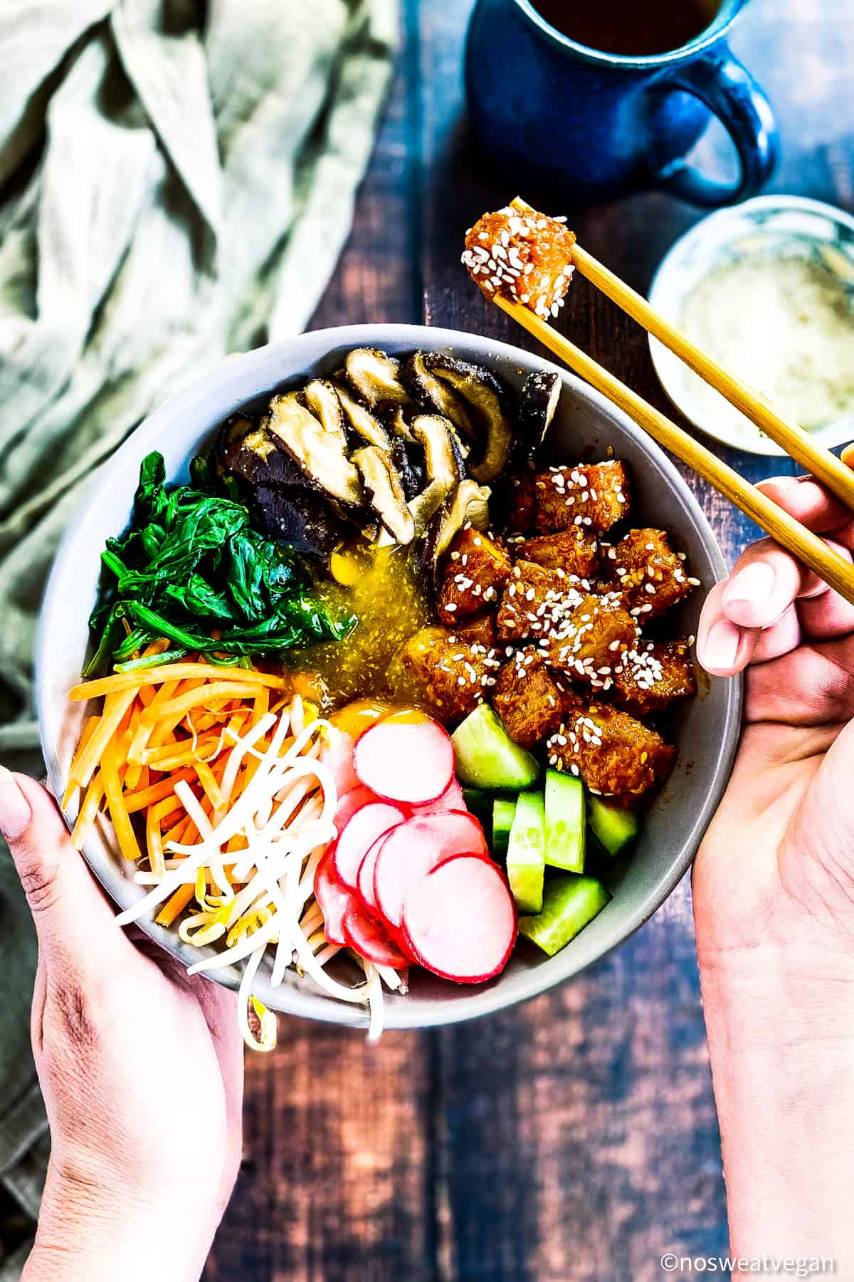 Bibimbap vegan ingredients in bowl with hand holding chopsticks and picking up a piece of Korean tofu.