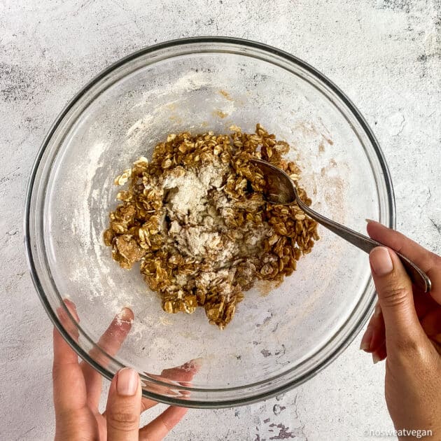 Hands mixing oat crumble topping in a bowl.