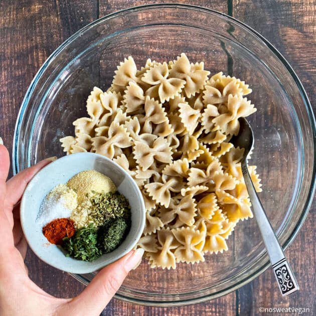 Cooked pasta in bowl with spoon and a hand holding little bowl of ranch seasoning.