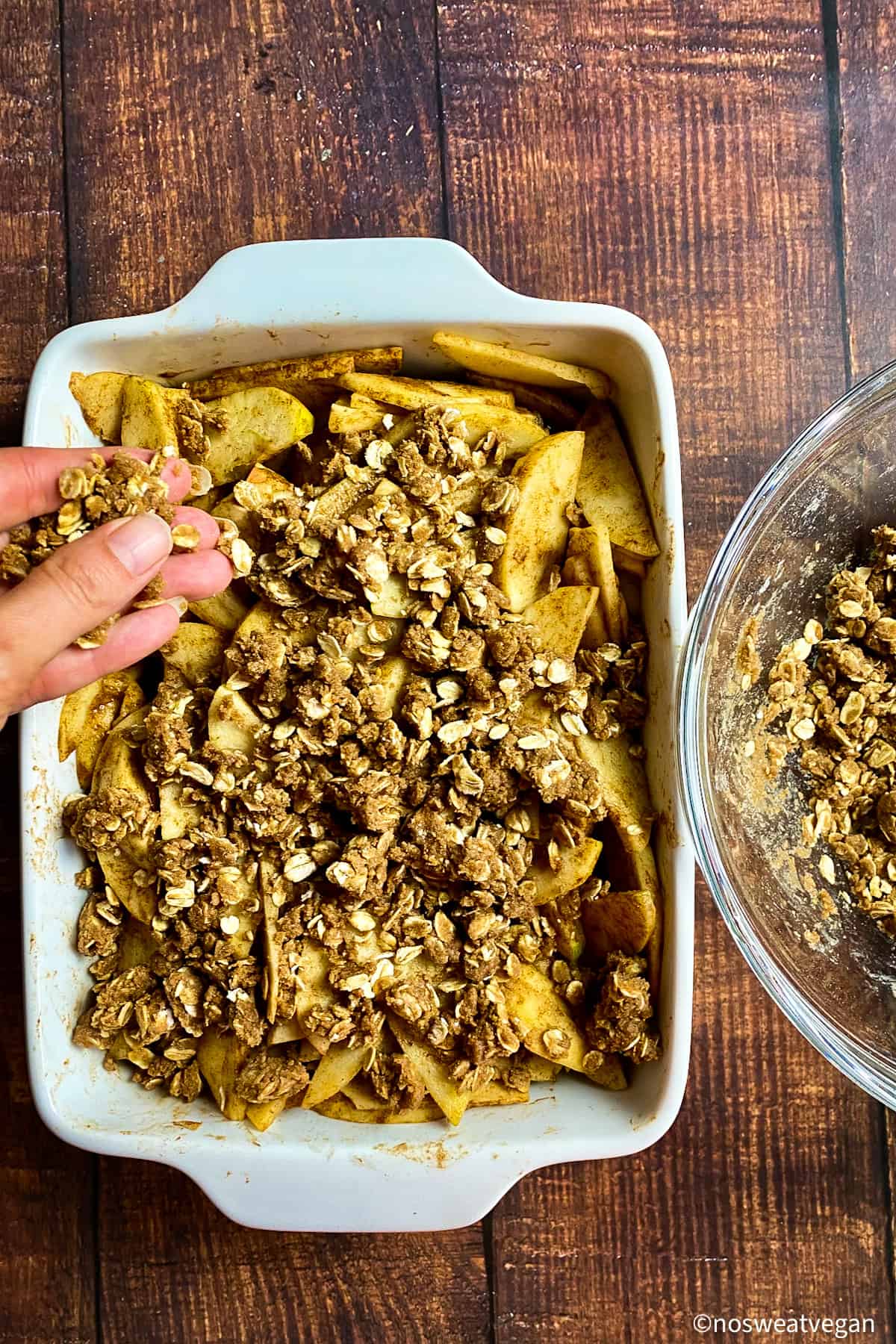 Hand adding crumble topping to partially cooked apples.