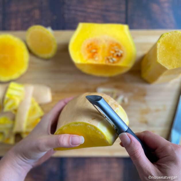 Hands peeling butternut squash.