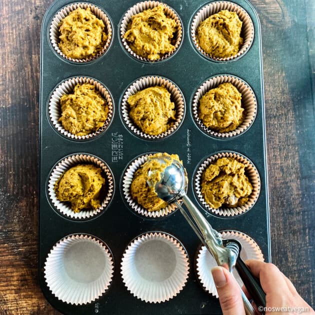 Hand scooping pumpkin muffin batter into muffin tins.
