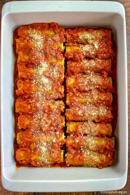 Uncooked cannelloni in pan covered in marinara sauce.