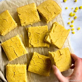 Best vegan cornbread on cooling rack with hand picking up a piece of cornbread.
