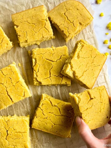 Best vegan cornbread on cooling rack with hand picking up a piece of cornbread.