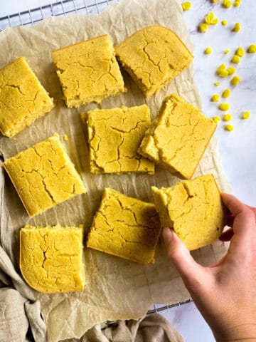 Vegan cornbread on a drying rack with hand picking up one piece.