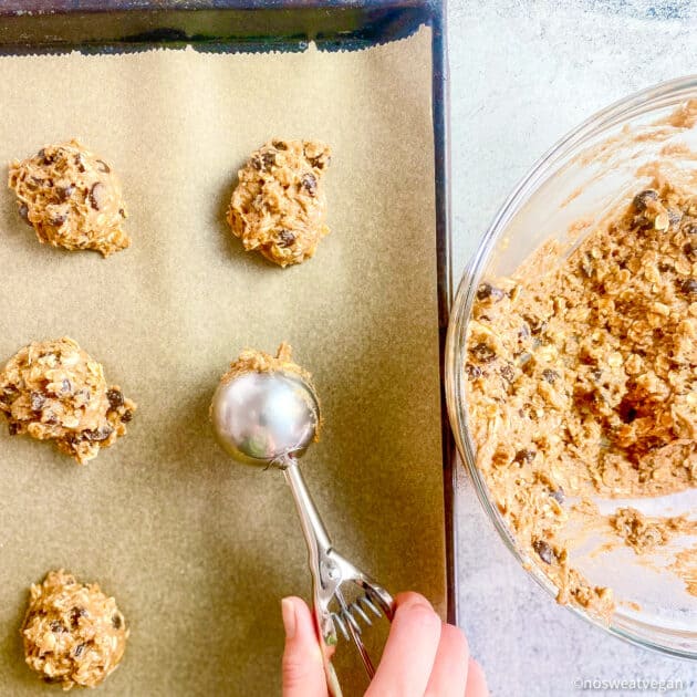 Hand scooping vegan oatmeal cookie batter onto baking sheet.