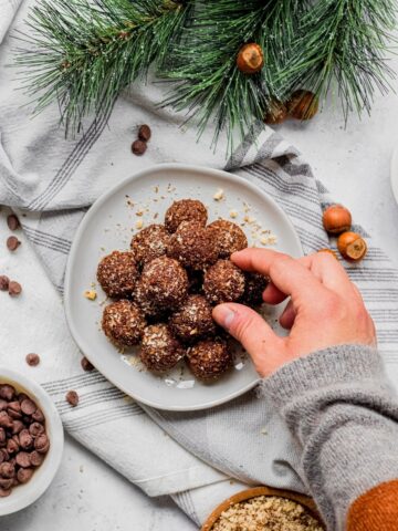 Chocolate hazelnut balls on plate with hand taking one.