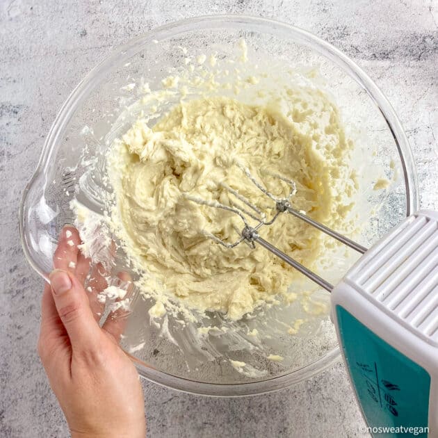 Creamed butter, sugar, and cream cheese in a bowl with hand mixer.