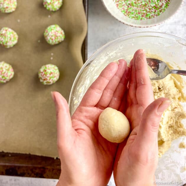 Hands rolling balls of cookie dough.