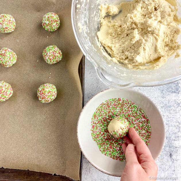 Hand rolling cookie dough ball in Christmas sprinkles.