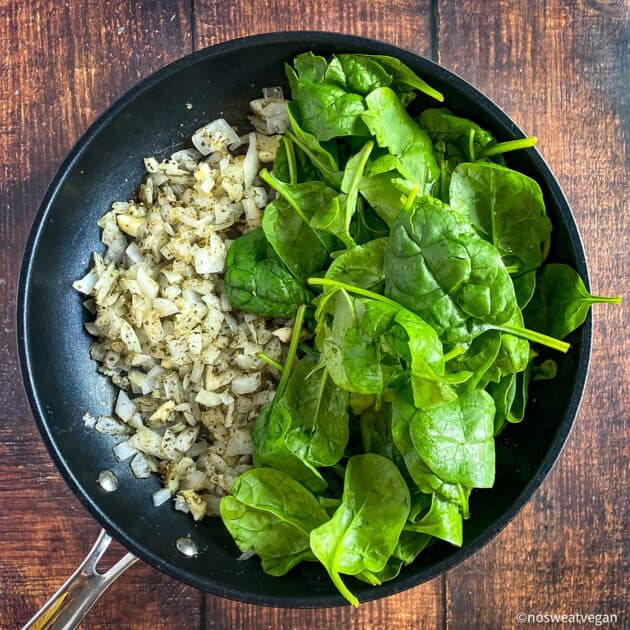 Cooked onions and raw spinach in skillet.