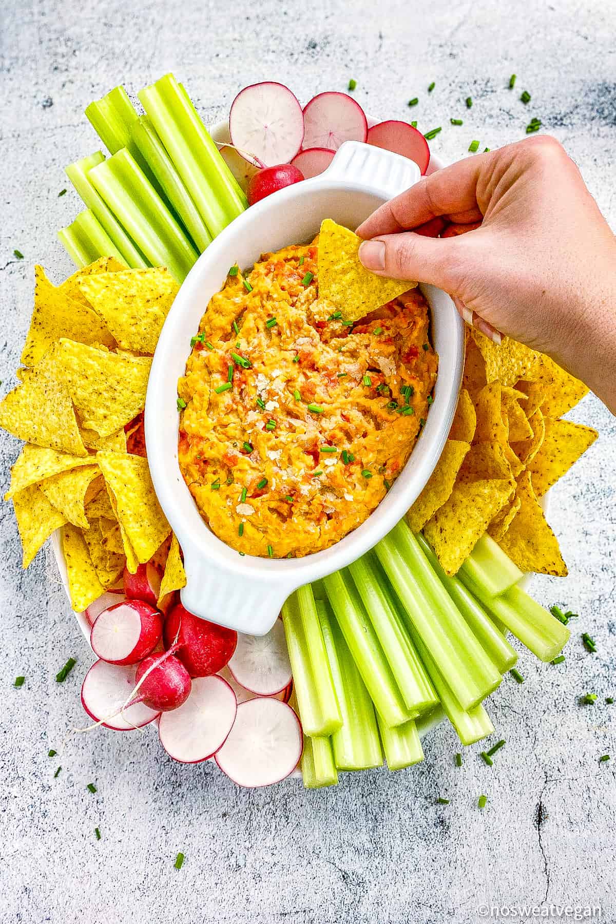 Hand dipping chip into vegan dip.