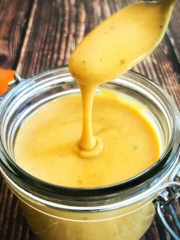 Vegan honey mustard dressing in a jar with spoon lifting up.