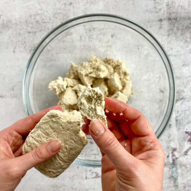 Hand breaking tofu into chunks over bowl
