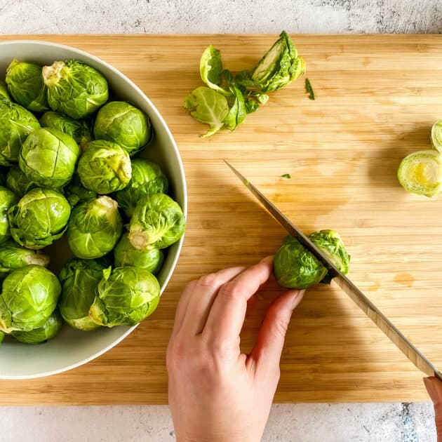 Hand holding a Brussels sprout to cut off the stem.