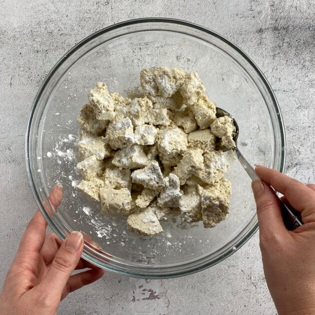 Hand mixing cornstarch into tofu chunks.