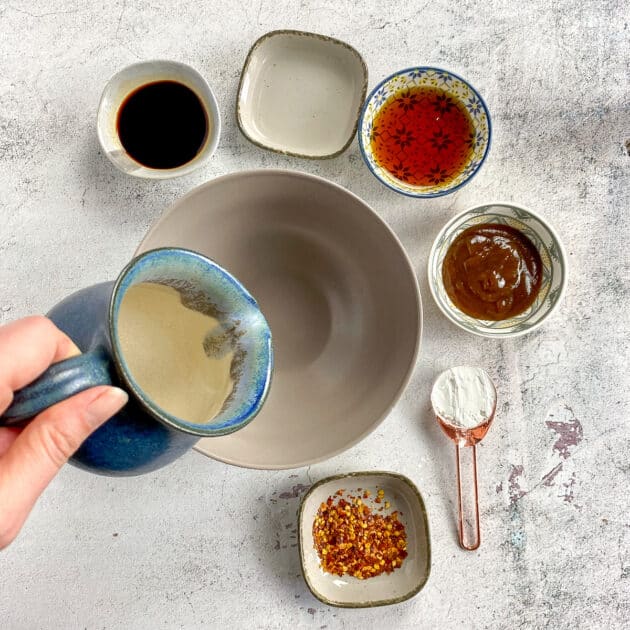 Hand adding water to bowl. Other ingredients for General Tso's sauce around bowl.