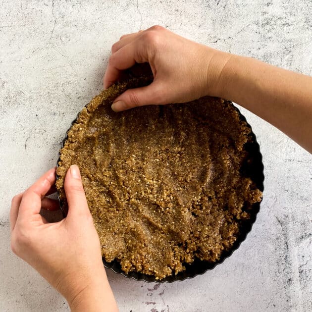 Two hands pressing the crust into the sides of the tart pan.