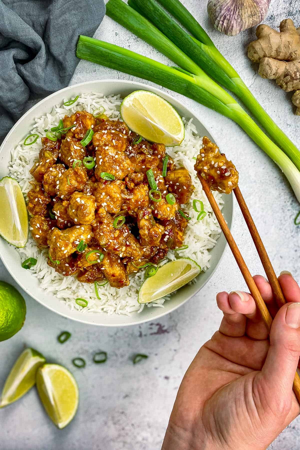 Hand using chopsticks to pick up a piece of vegan general tso chicken from a bowl.