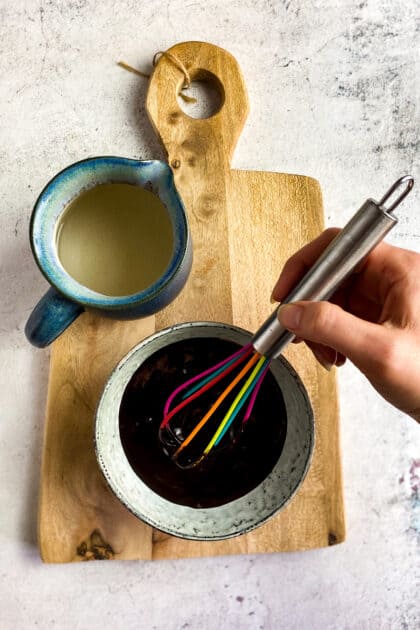 Hand mixing quick chocolate sauce with a whisk next to a pitcher of water.