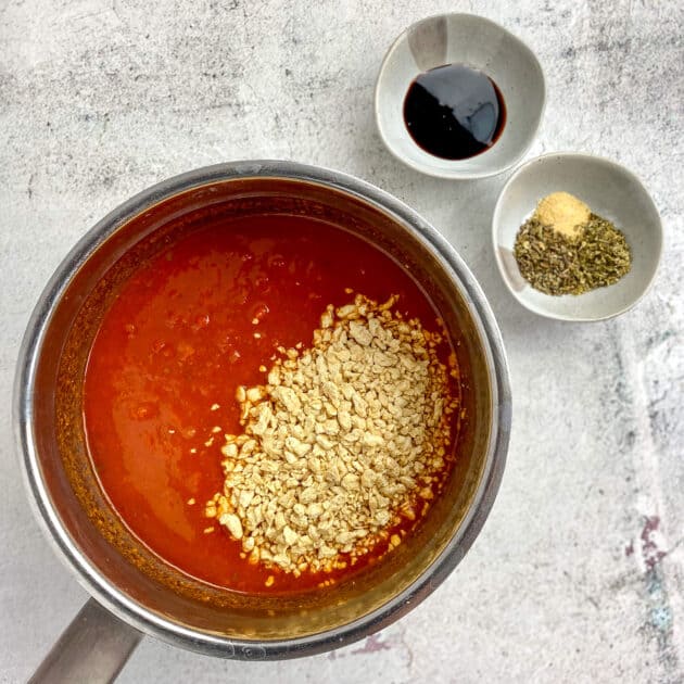 Pot with sauce and tvp. Seasoning and balsamic glaze in bowls on the side.