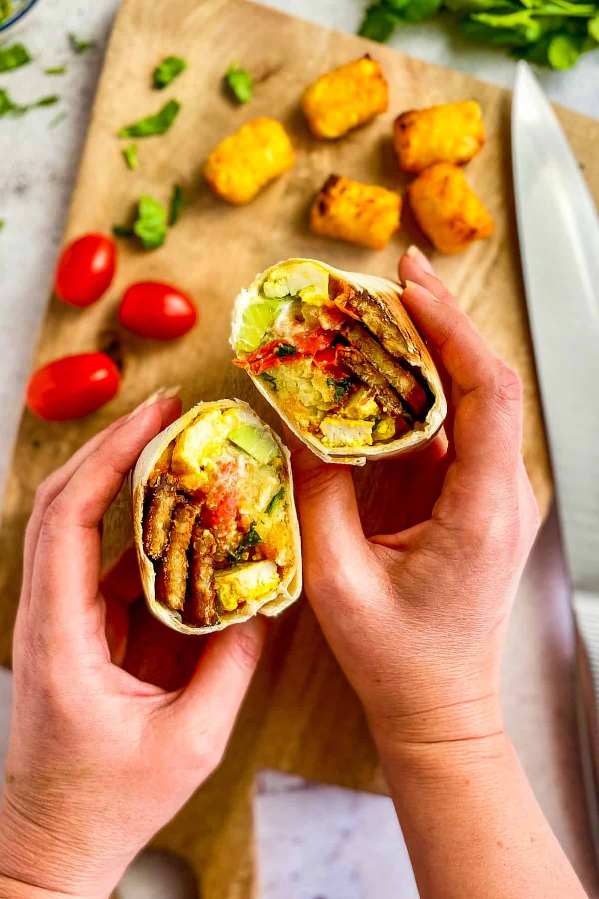 Two hands holding a plant-based breakfast burrito that has been cut in half.