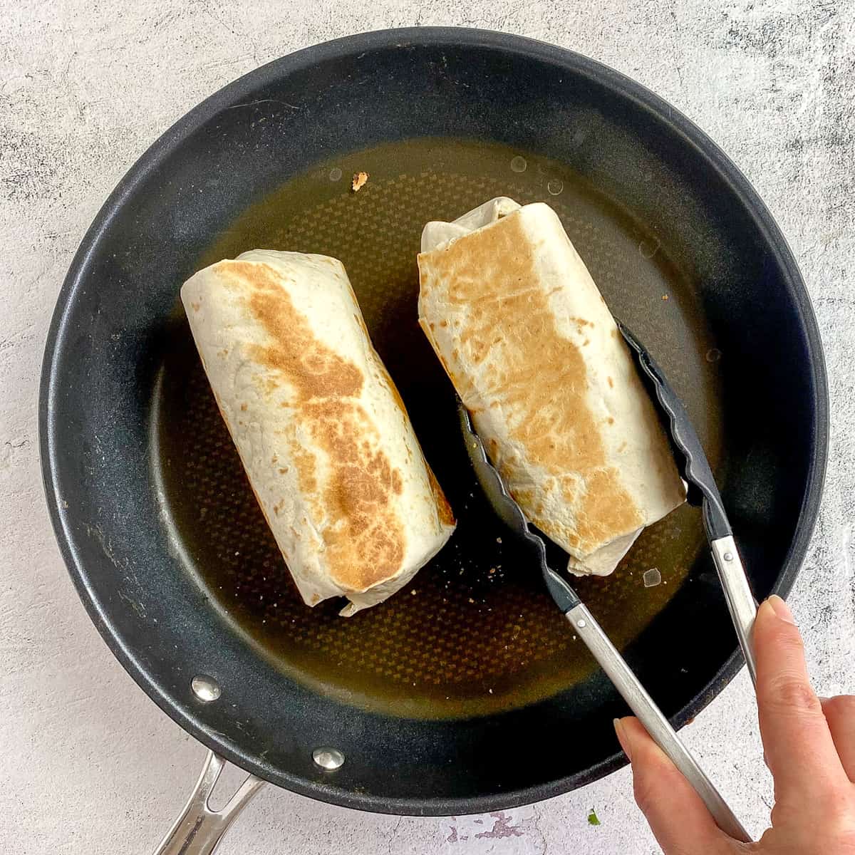 Two vegan breakfast burritos seared in skillet.