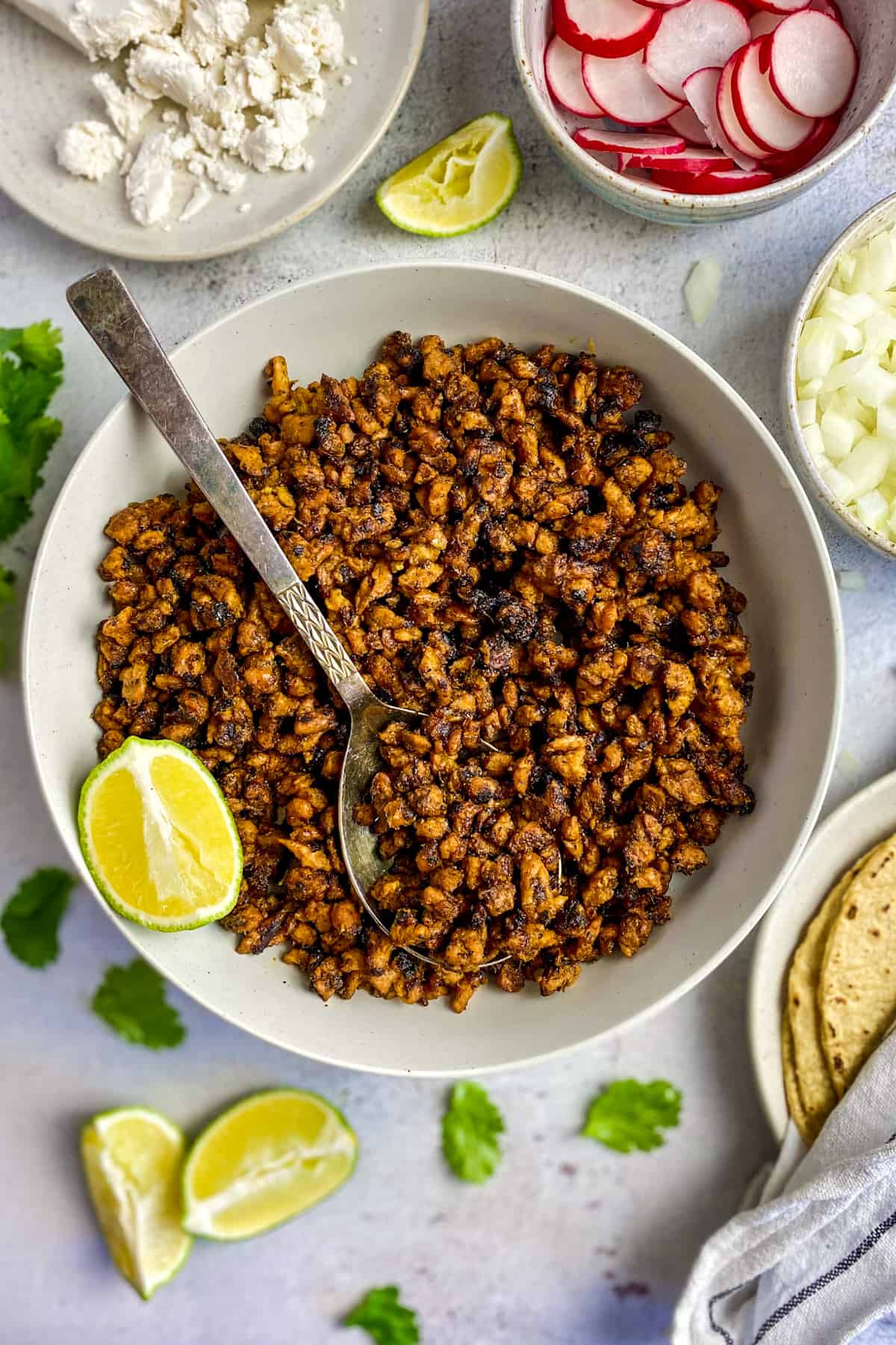 Vegan carne asada in a bowl surrounded by toppings.