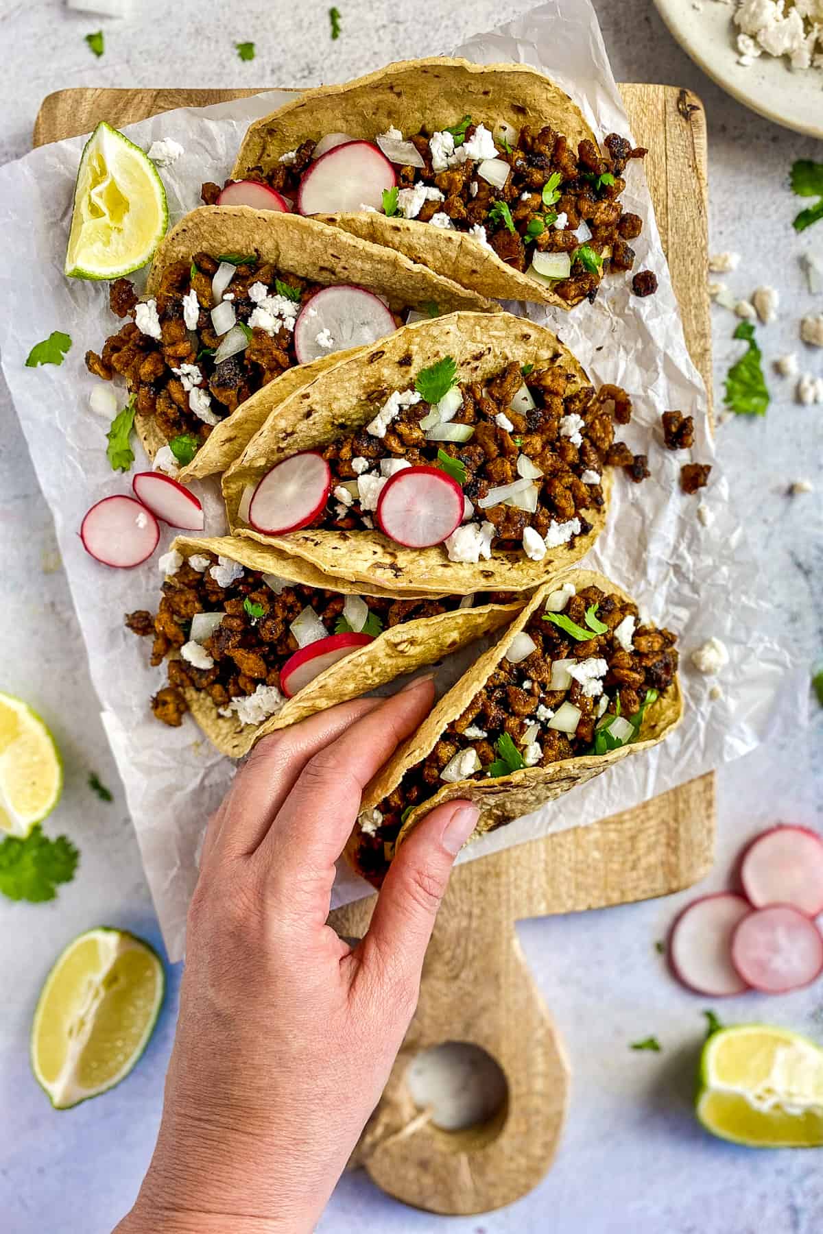 Vegan carne asada tacos on a cutting board with hand taking one.