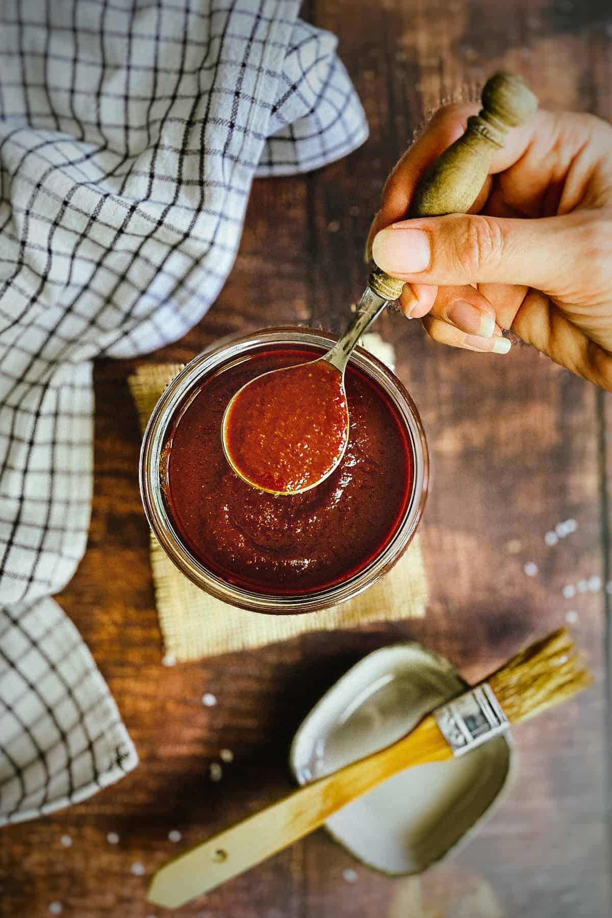 Vegan bbq sauce in jar with hand holding up spoon.