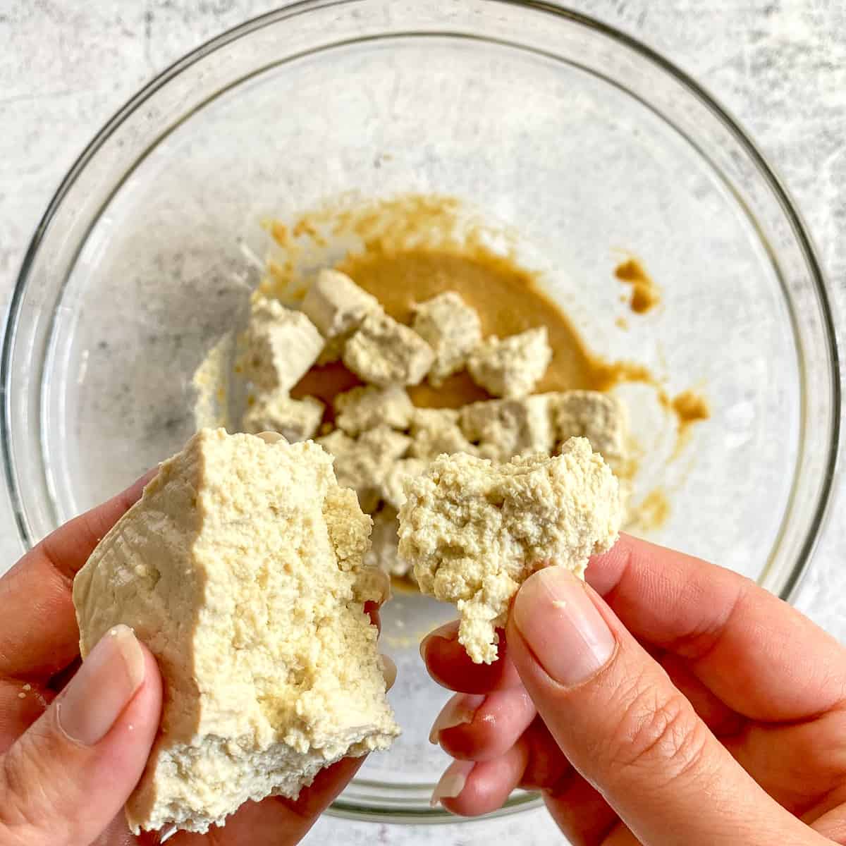 Hands breaking tofu into chunks.