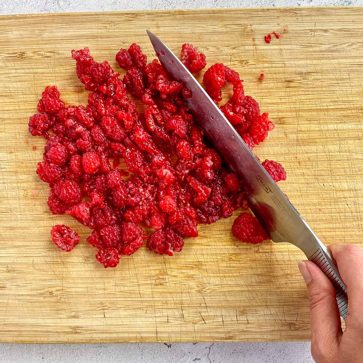 Hand chopping raspberries on a cutting board.